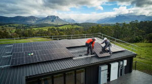 Solar installers fitting rooftop panels on a Tasmanian home with Tesla Powerwall battery storage and mountain views